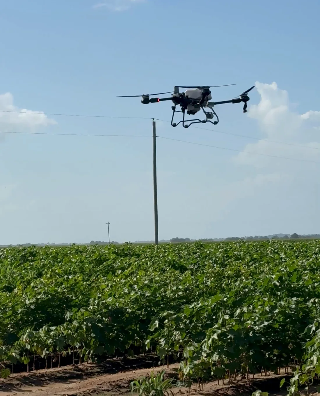 Talos agricultural drone in flight over crops with field and equipment in the background